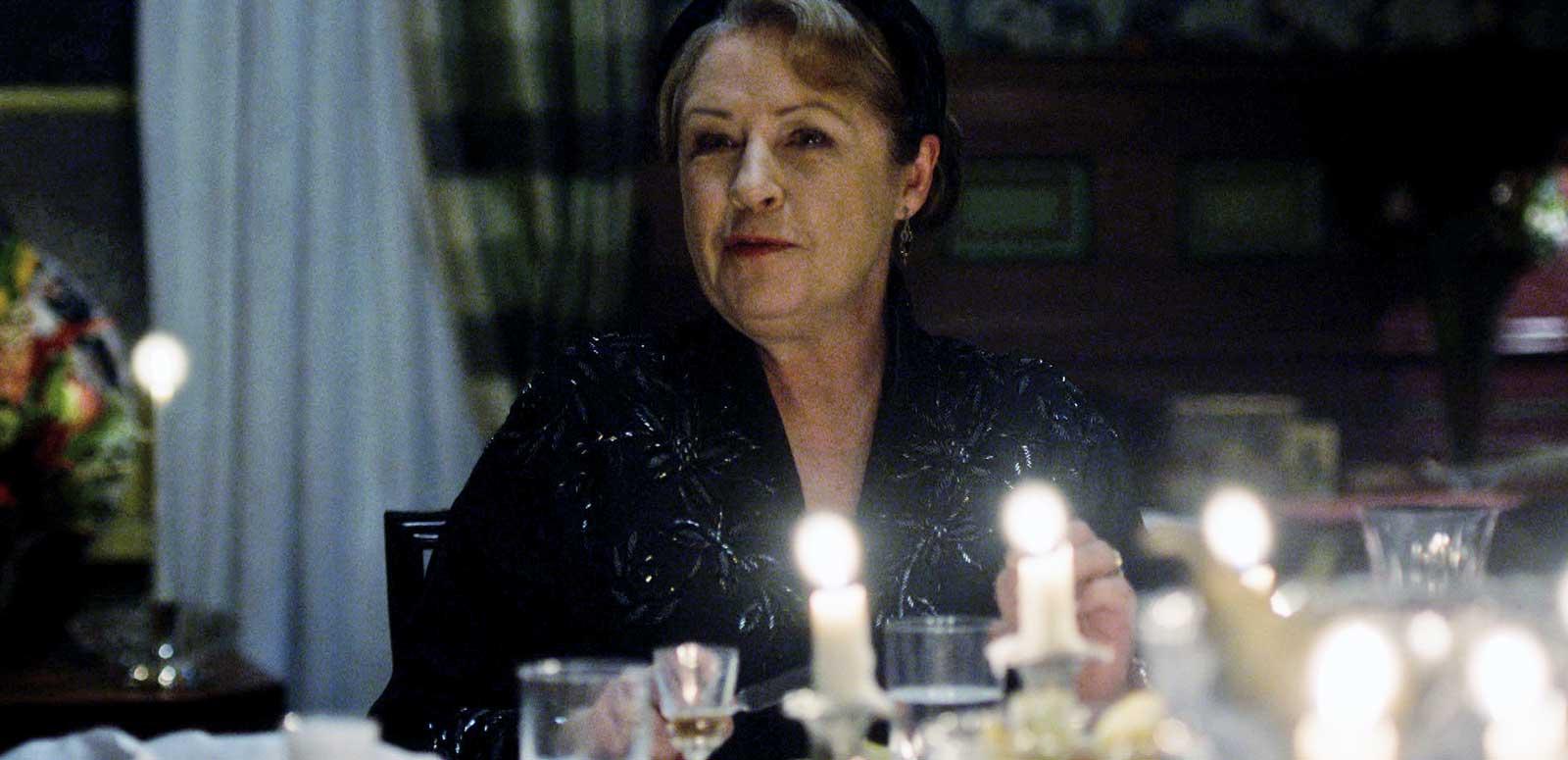Actor Noni Hazelhurst dressed in black and seated at a dinner table in a scene from the show A Place to Call Home
