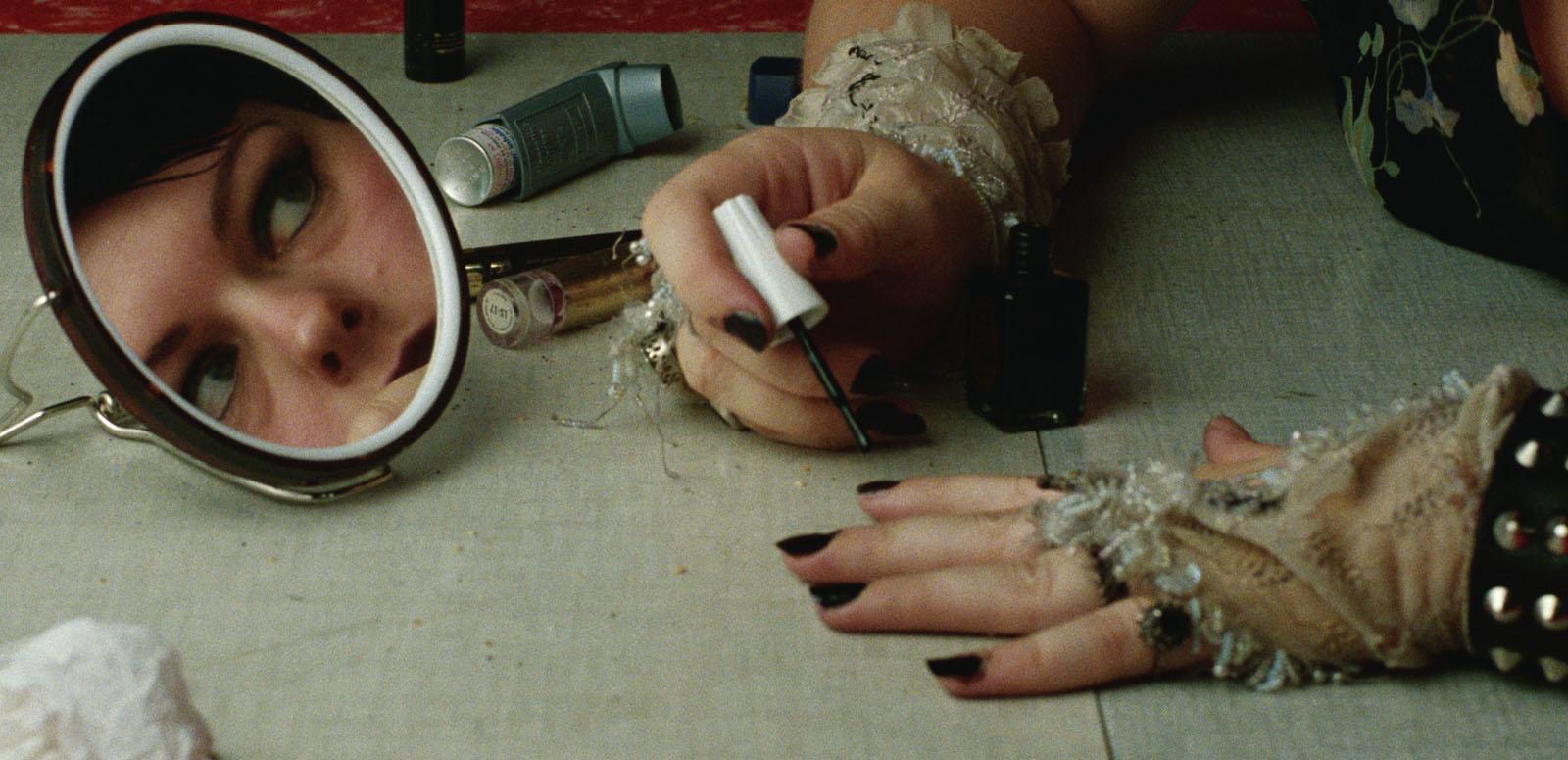 Genevieve Lemon's face is reflected in a small mirror while she applies black fingernail polish.