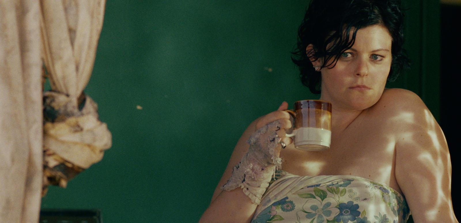 Genevieve Lemon holding a coffee mug and looking out the window in a still from the film Sweetie.