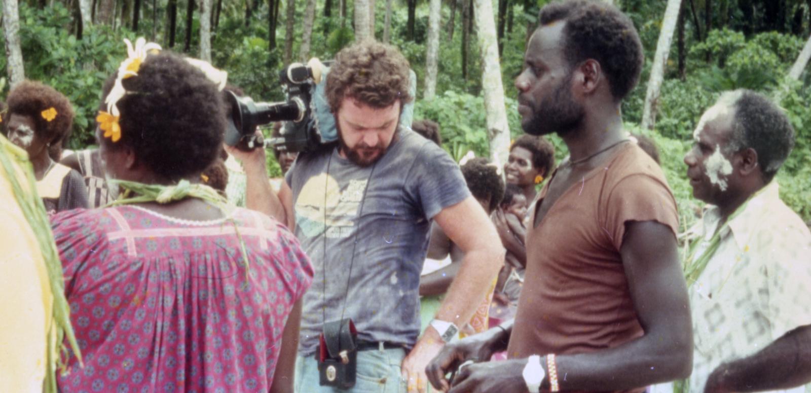 Co-director Chris Owen holds a film camera on his shoulder and stands next to co-director and star Albert Toro and other actors on location for the 1982 film Tukana in the Papua New Guinea Highlands.