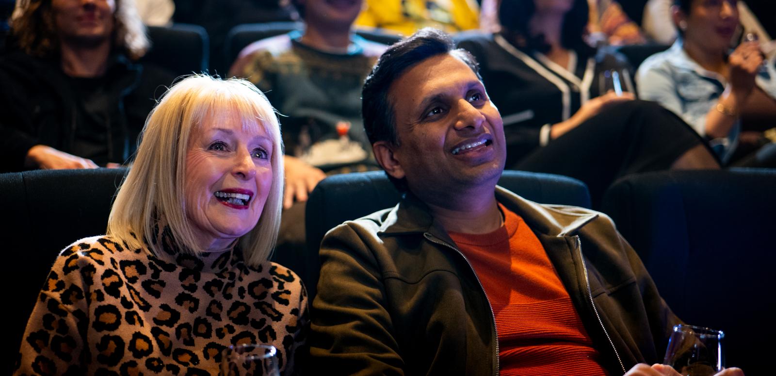 Older couple sitting in cinema seating looking up at screen. 