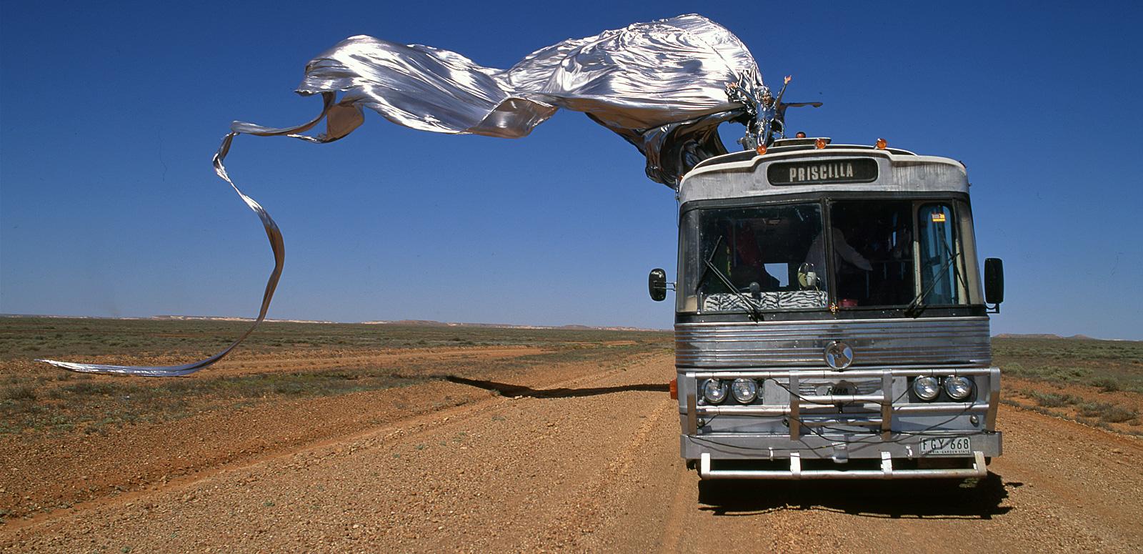 Guy Pearce in drag miming to an opera aria on top of a bus travelling through the desert