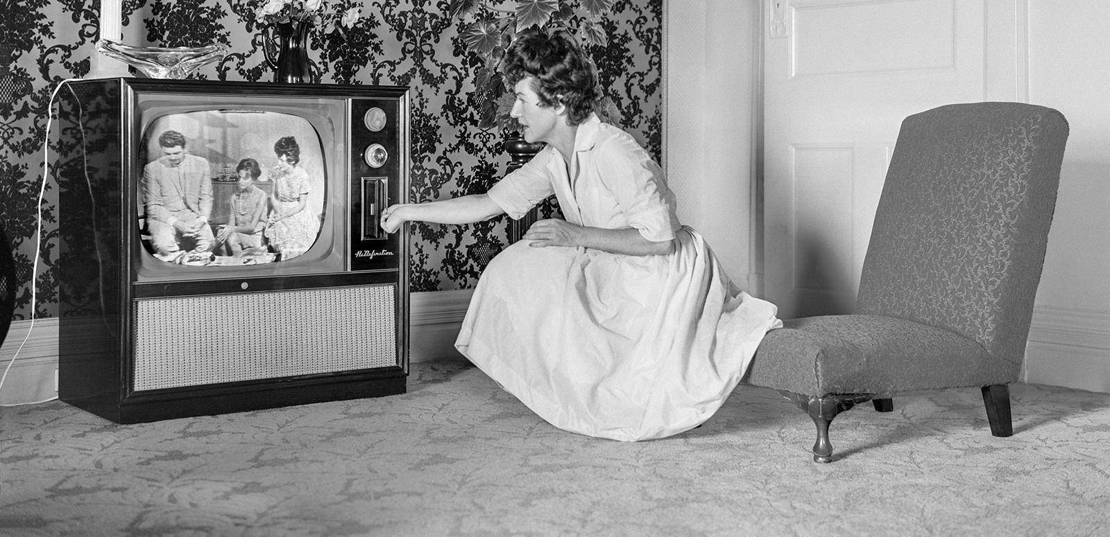 A woman kneeling down to adjust a television, c1950s.