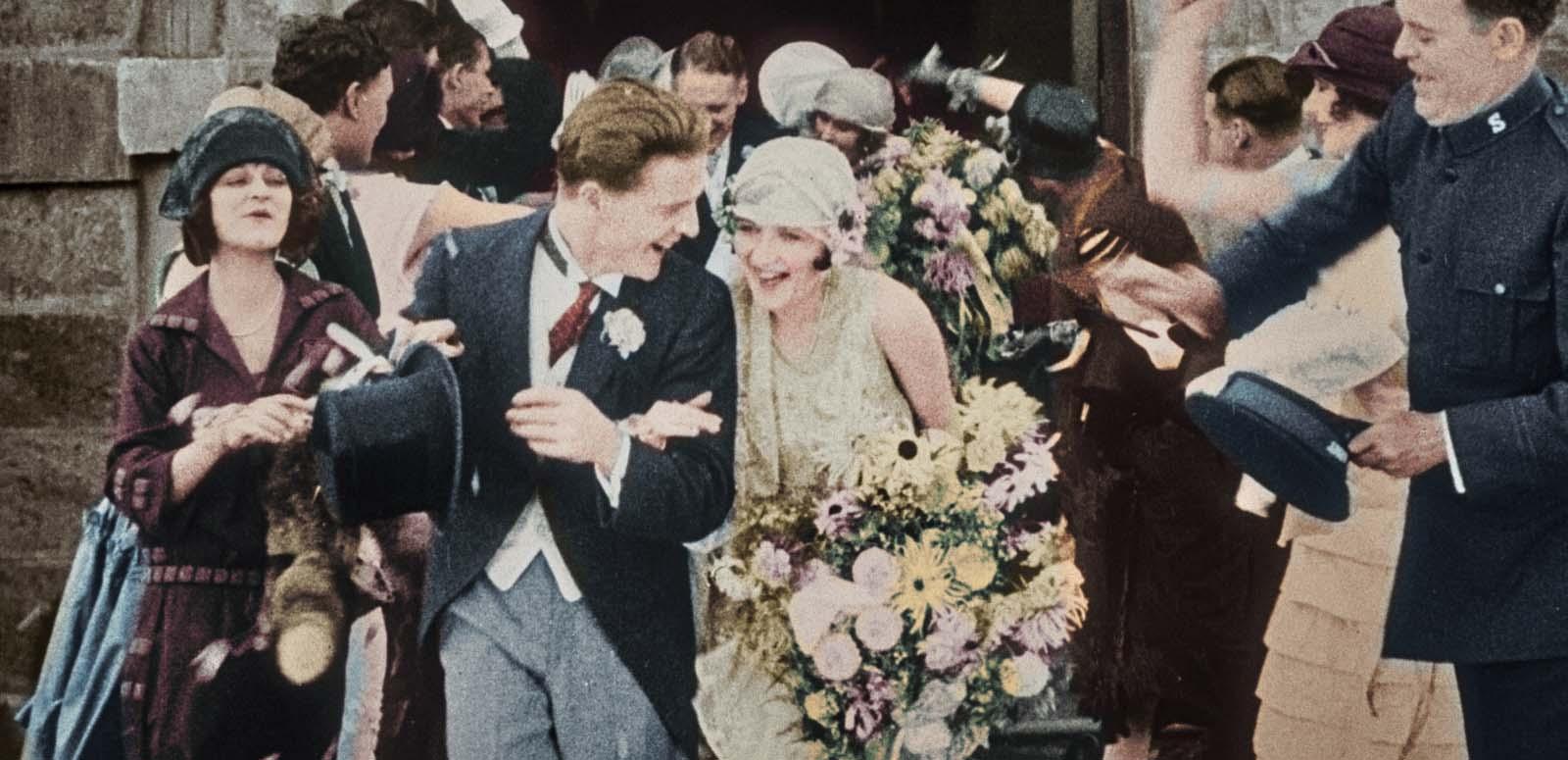 The celebrating bride and groom and wedding party exit the church after a wedding in 1925