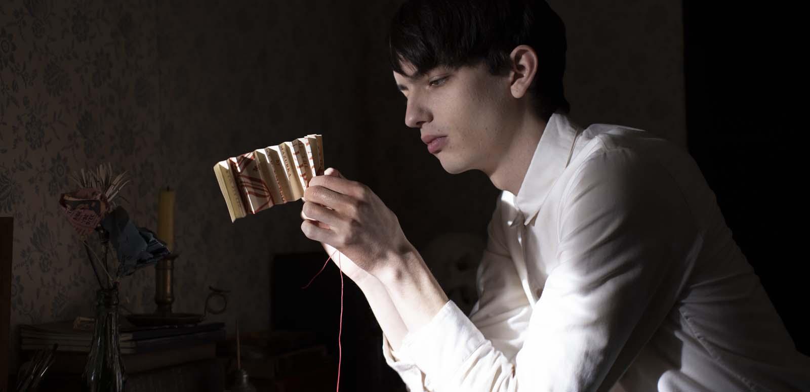 Kodi Smit-McPhee folding paper to make it into decorative flowers in a scene from The Power of the Dog