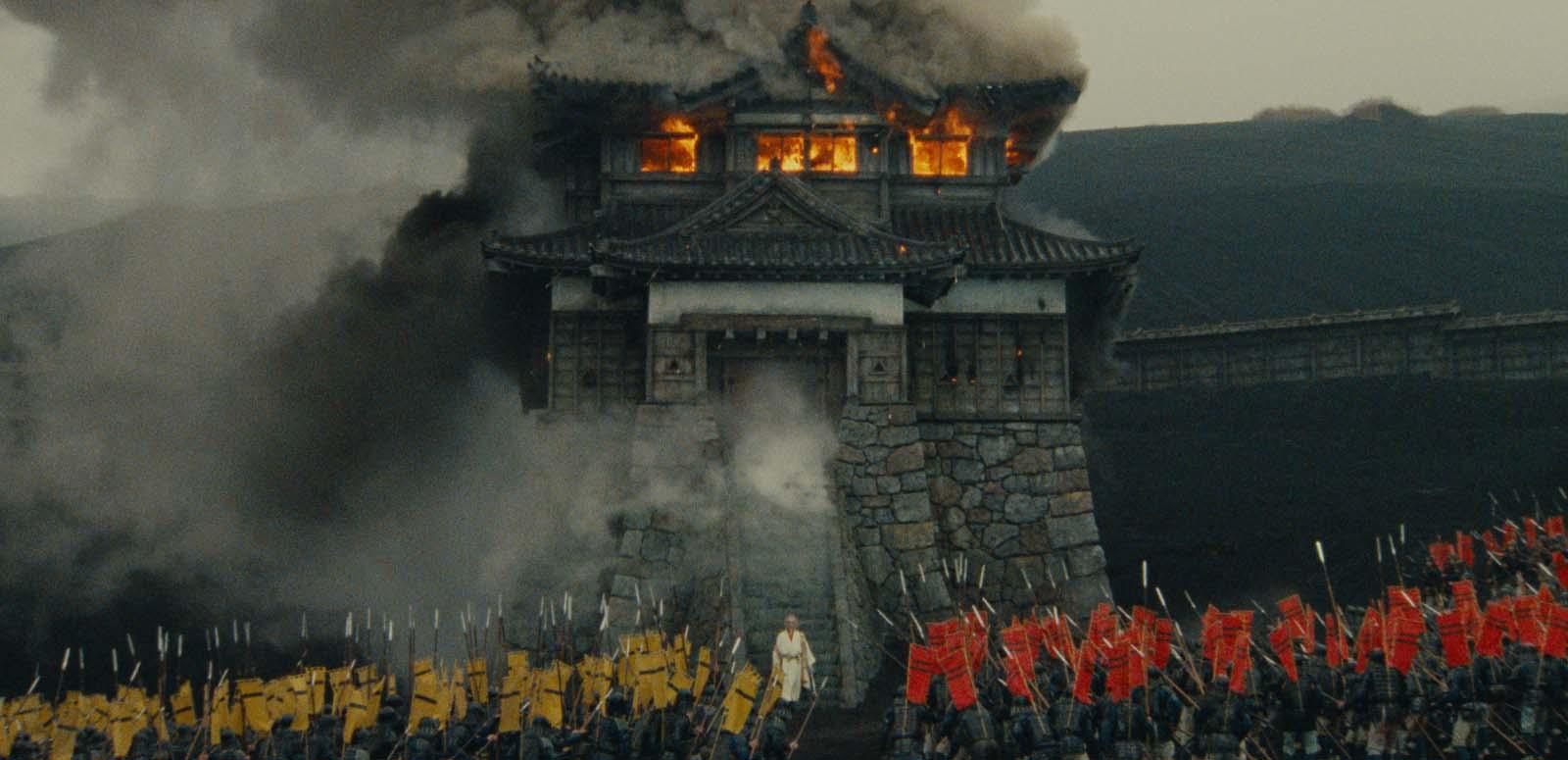 Film still from the movie RAN Film still from RAN of a Japanese castle on fire surrounded by an army.