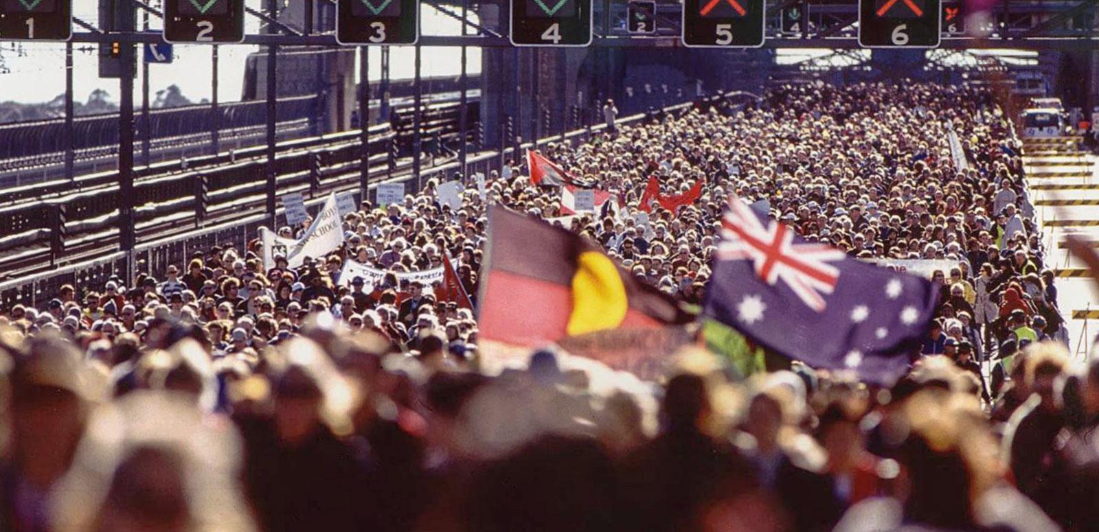 Huge crowd on the Sydney Harbour Bridge during the Walk for Reconciliation. Some people are waving Australian and Aboriginal flags.