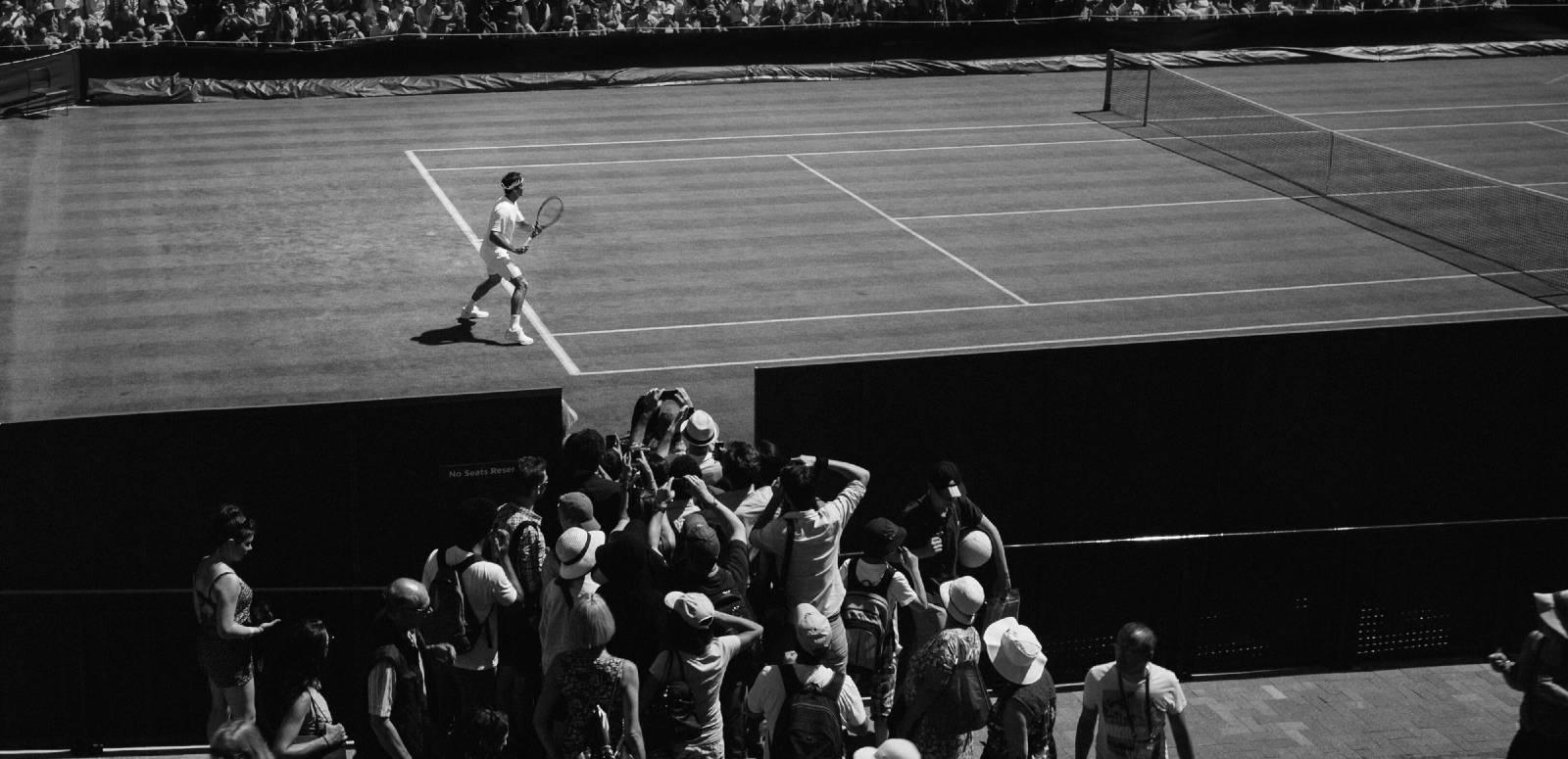 A male tennis player on the court at Wimbledon, watched by a scrum of press photographers