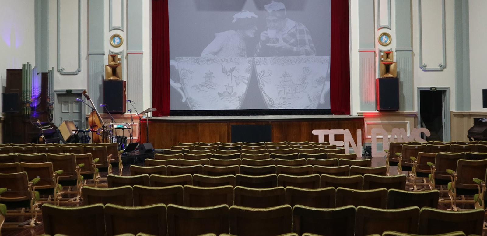 The interior of an old theatre. You can see the screen in the centre and rows of chairs facing it.