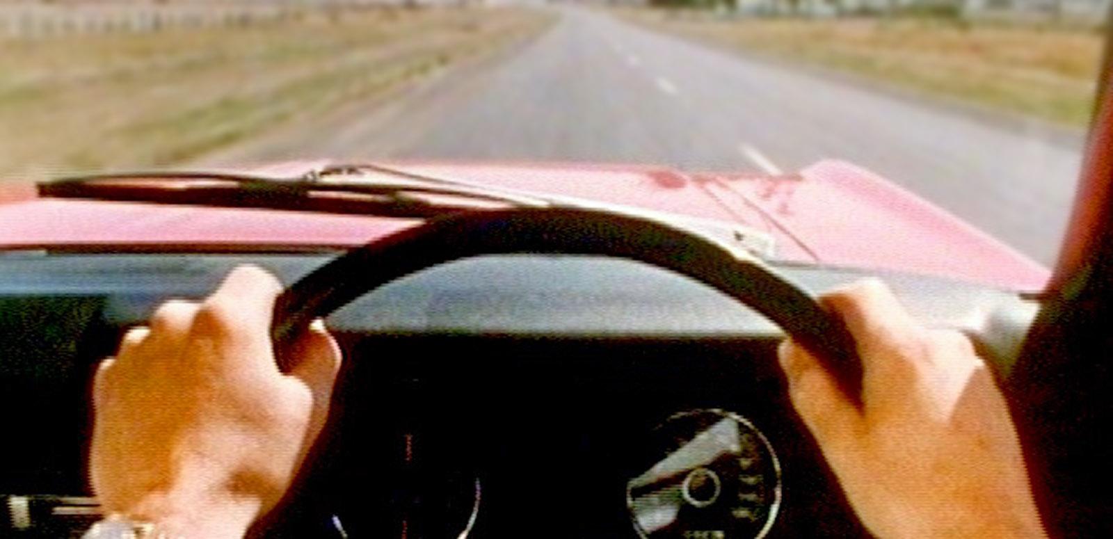 A man is behind the wheel of a red XT Falcon. We see his point of view of the road ahead.