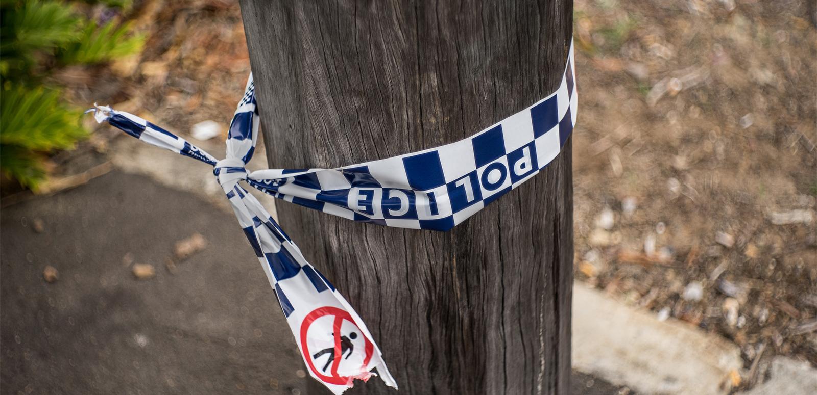 True Crime - Police tape A section of a telegraph pole on a sidewalk with some blue and white chequered police tape tied around it.