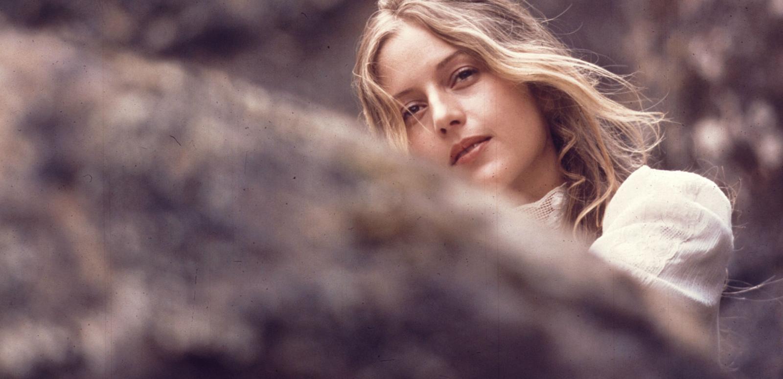 Anne Louise Lambert as Miranda, peering over a rock and looking into the distance in a scene from Picnic at Hanging Rock.