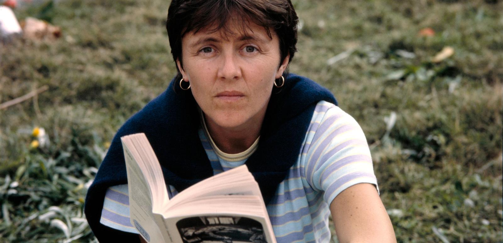 Helen Garner, author of 'Monkey Grip' Helen Garner sitting in the ground, look at the camera and holding an open book