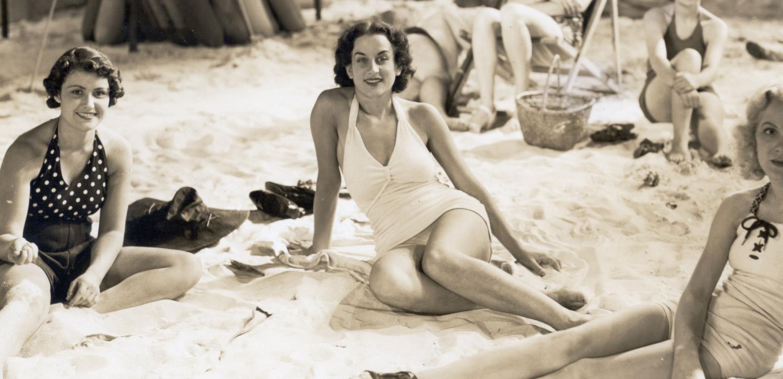 Women in swimsuits lounging on a film set made to look like a beach.