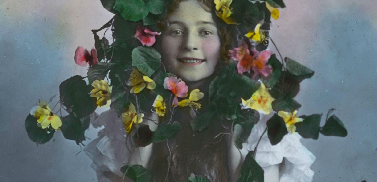 Glass slide image of a young girl peering through the centre of a wreath of flowers.