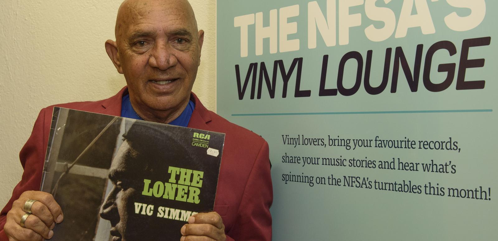 Vic Simms at the Vinyl Lounge Vic Simms holding a copy of his record The Loner in front of the Vinyl Lounge banner