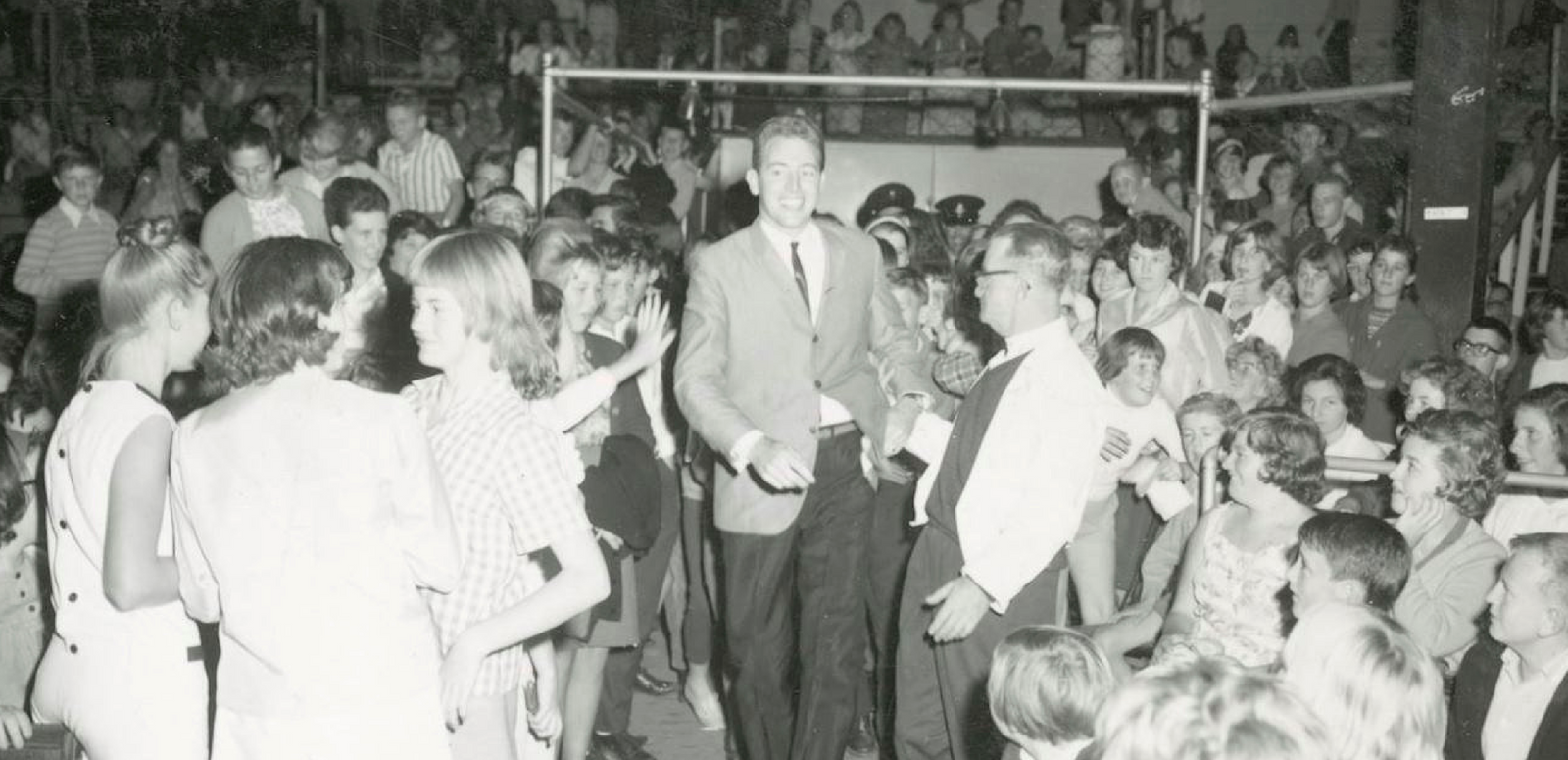 Popstar and TV personality Jimmy Hannan walking down the aisle at the Sydney Stadium with a crowd of people around him.