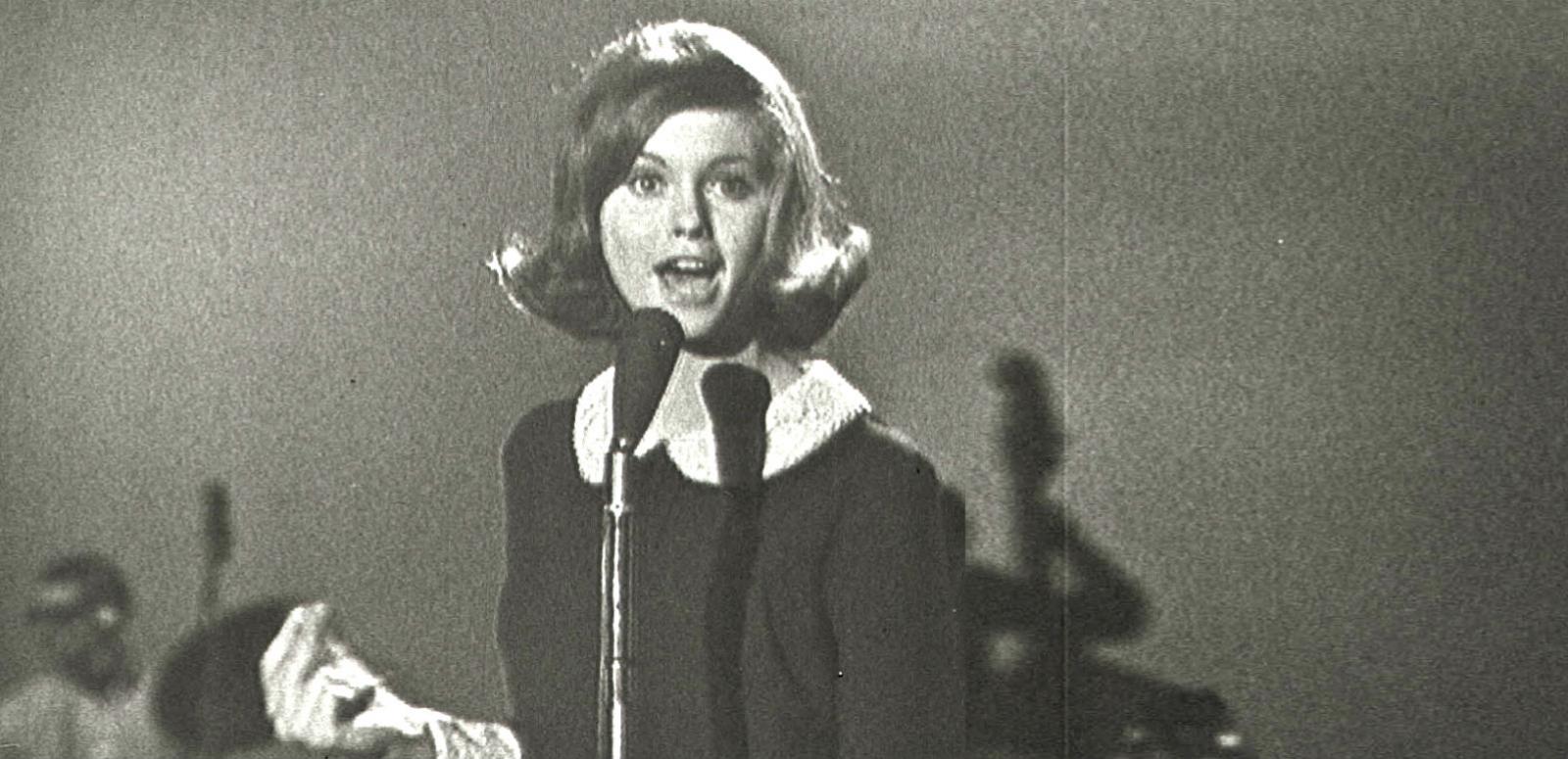 World TV Day - Olivia Newton-John - Hero image Olivia Newton-John at age 16 in a TV studio standing behind a microphone singing.