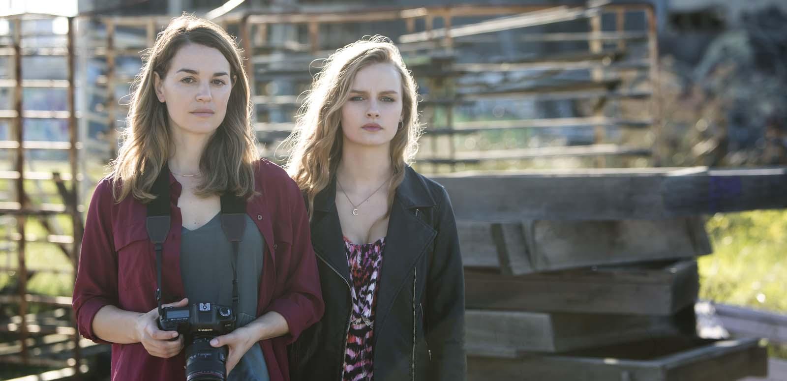 Two women standing in front of a building site. One woman is slightly older and is holding a camera.