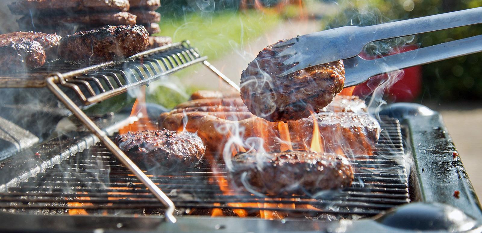 Close up of a barbecue grill with burger patties cooking on it.