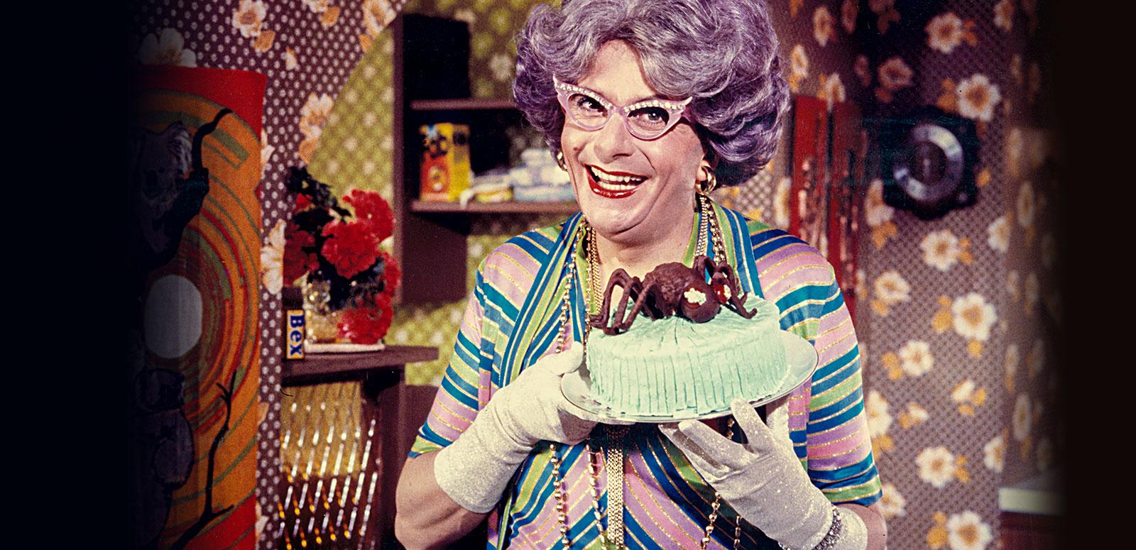 Dame Edna Everage collection hero Dame Edna Everage is in a very colourful kitchen. She (Barry Humphries in drag) is holding an iced cake with a chocolate spider on top. She has wisteria-coloured hair and sparkling pink glasses.