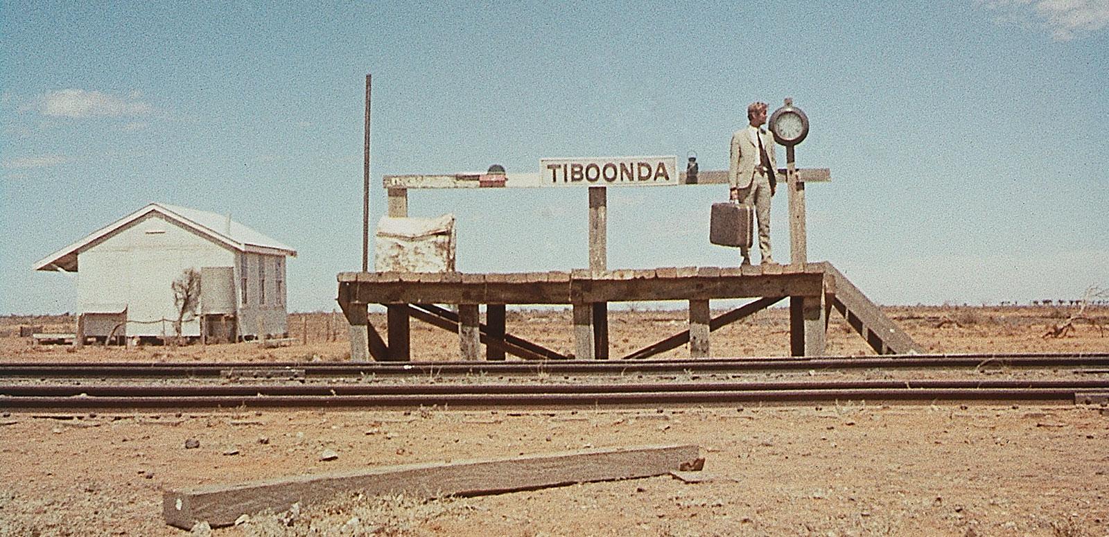 A man carrying a suitcase and wearing a light brown suit waits on a small outback railway platform A man carrying a suitcase and wearing a light brown suit waits on a small outback railway platform