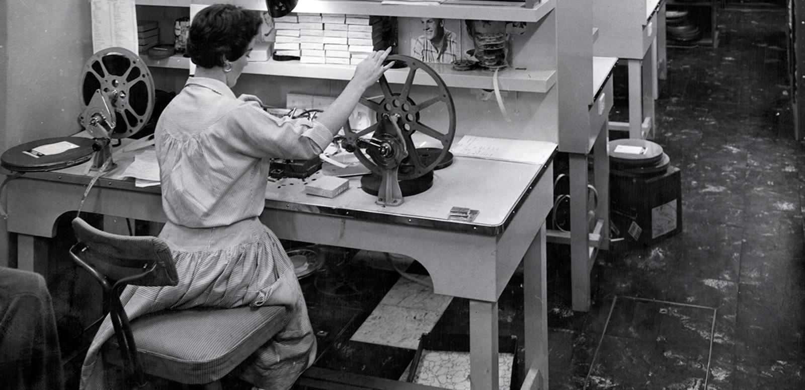A woman sitting with her back to the camera winding a film reel.