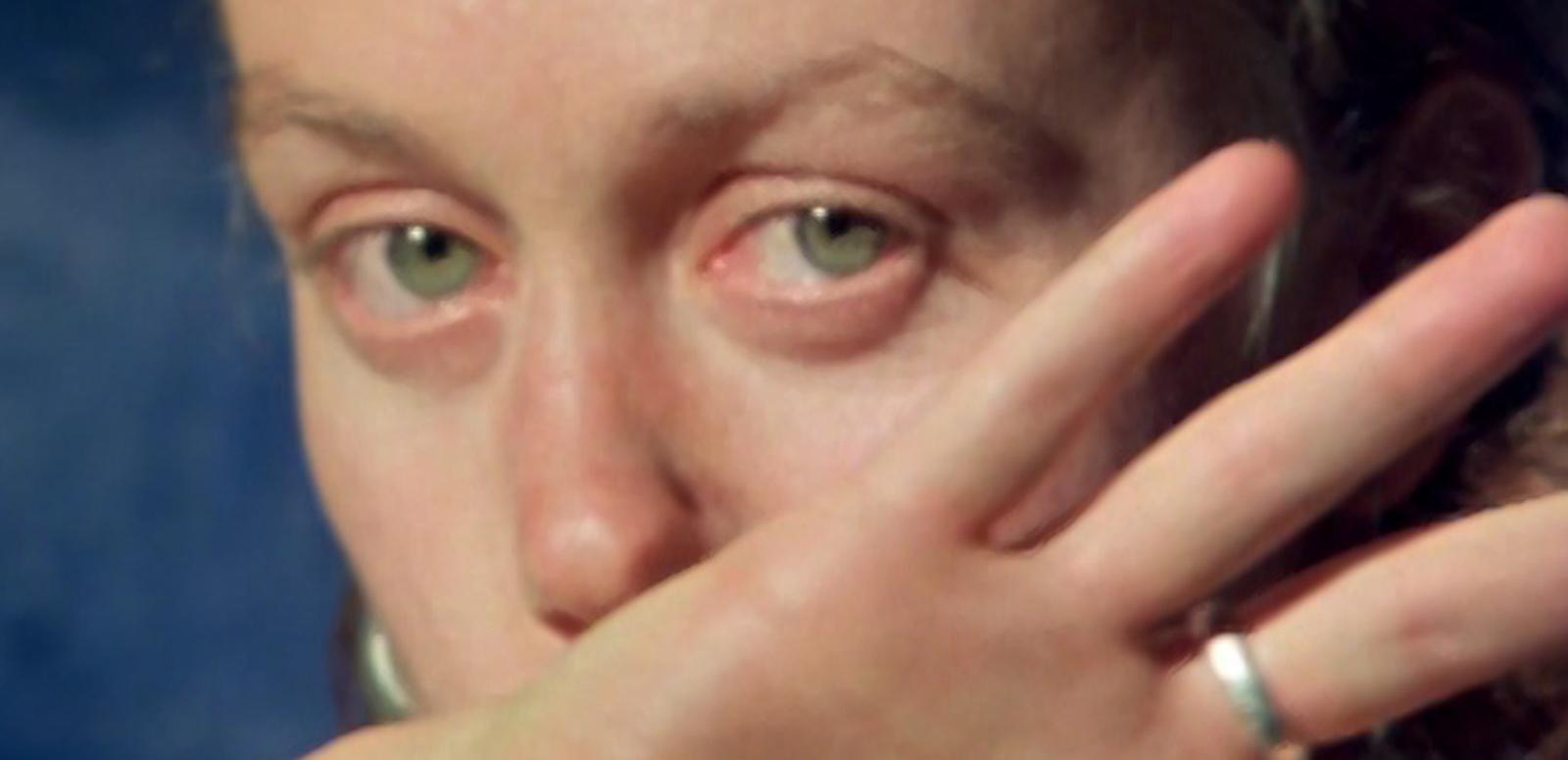 A woman looks at the camera as she wipes her face with her hand.