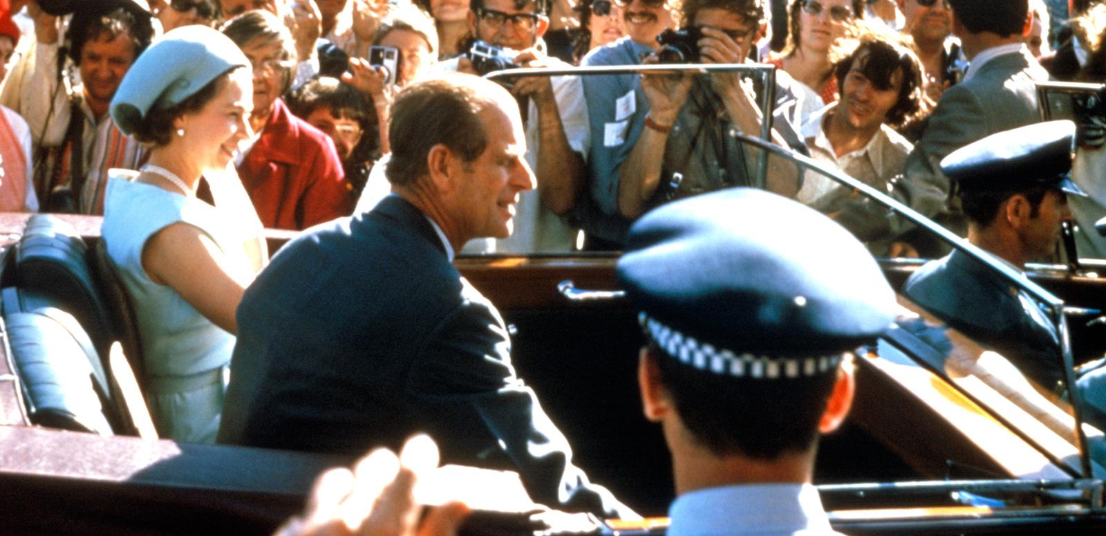 Queen Elizabeth and Prince Philip riding in the back of a car in Sydney in 1973, surrounded by members of the public and photographers. 