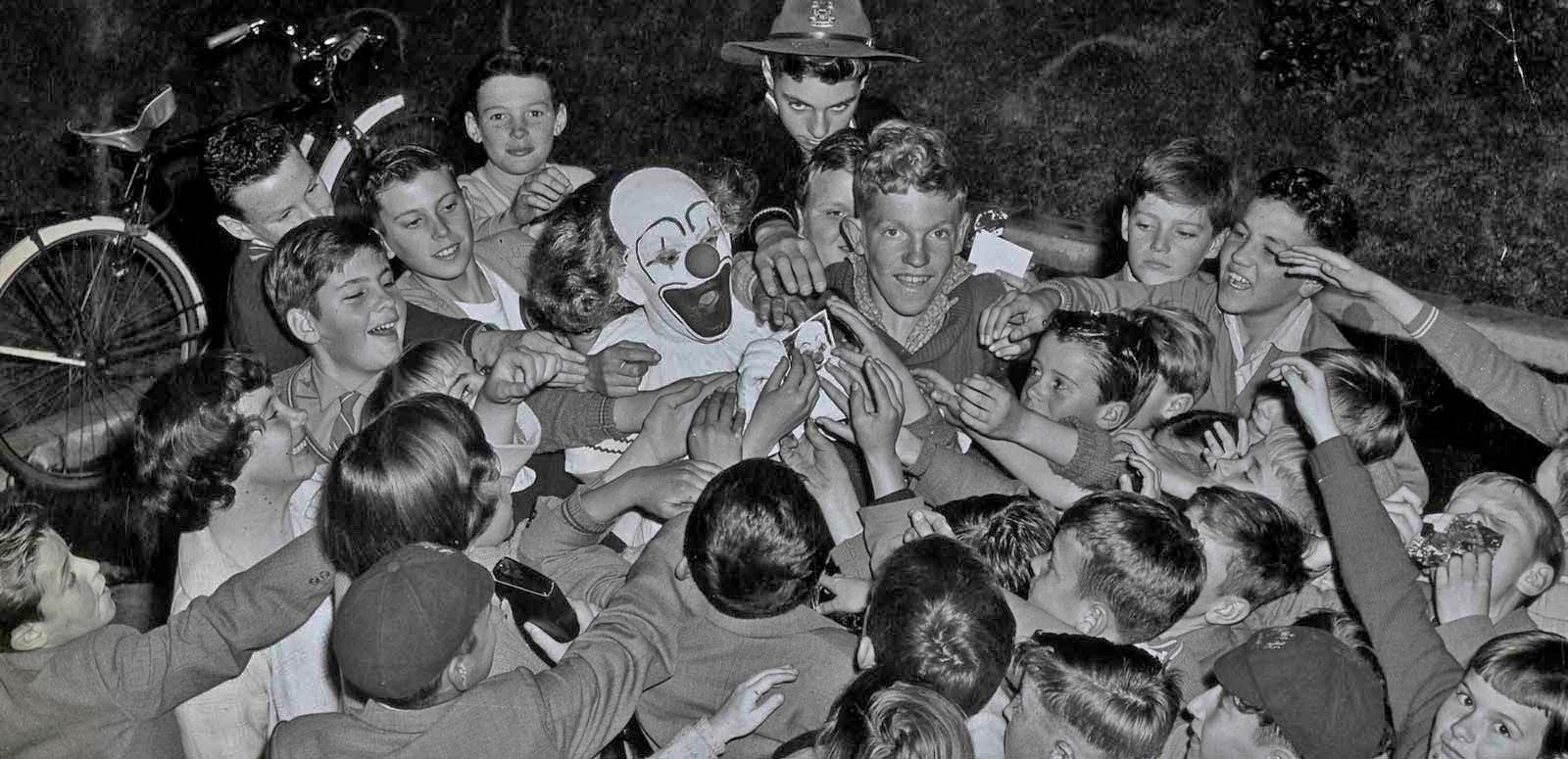 Bobo the clown is surrounded by a crowd of children reaching out to touch him Bobo the clown is surrounded by a crowd of children reaching out to touch him