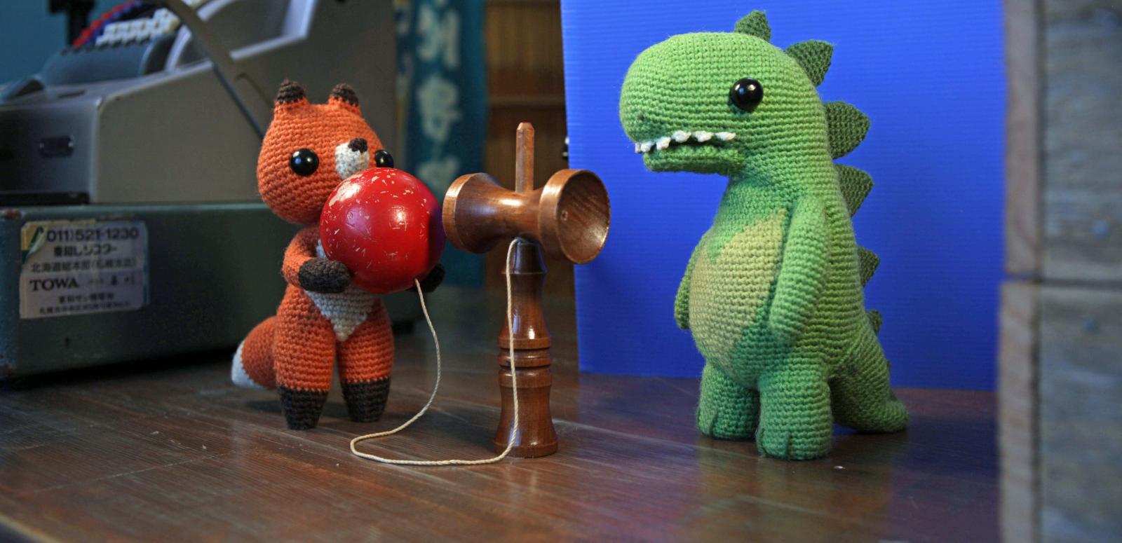 Animation still of a knitted dinosaur and a knitted fox