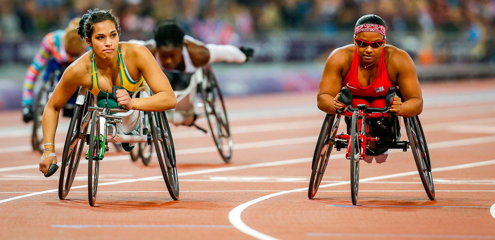 Wheelchair track athletes at the 2012 summer paralympics Women wheelchair athletes competing on an Olympic race track. There are two in the foreground who are side by side and another two can be seen further down the track.
