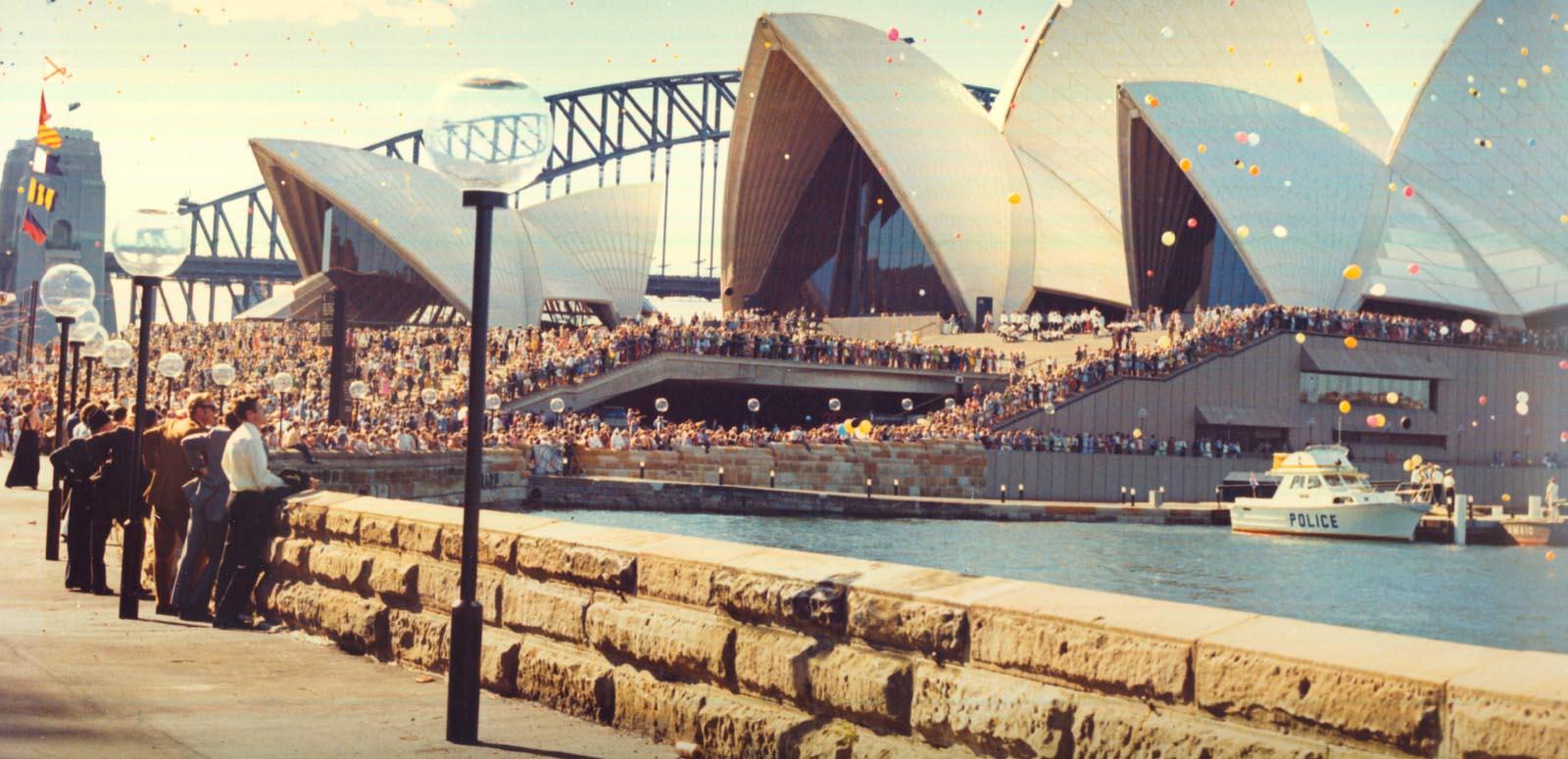 Fifth Facade: Opera House cover image People line the boardwalk and steps of the Sydney Opera House for its opening. There are balloons in the air and the Sydney Harbour Bridge is in the background.