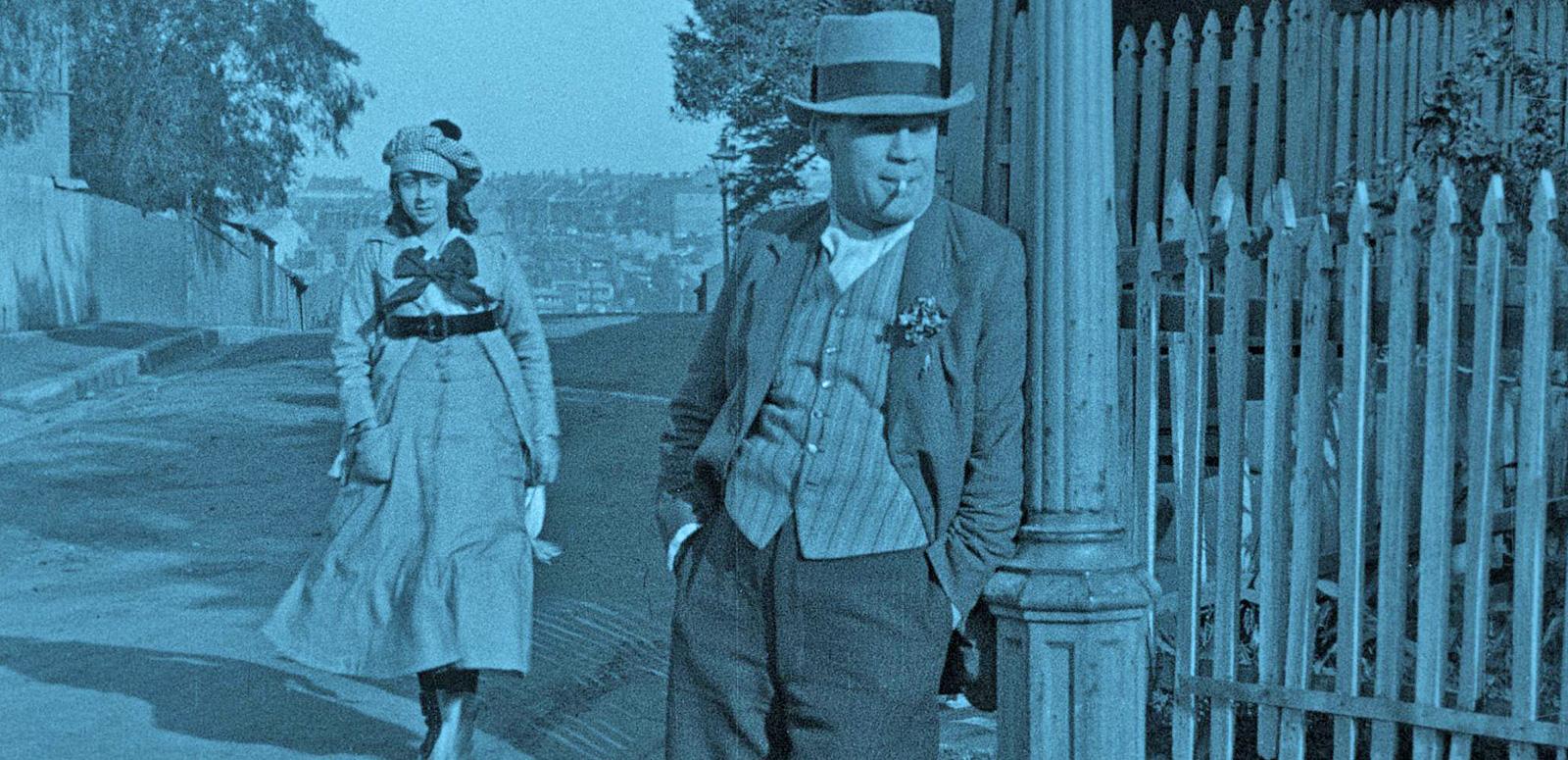 NFSA Restores Collection hero image_Sentimental Bloke A scene from the film The Sentimental Block featuring Arthur Tauchert as 'The Bloke' leaning against a lamp post on a street corner Actress Lottie Lyell (Doreen) is walking up the street behind him.
