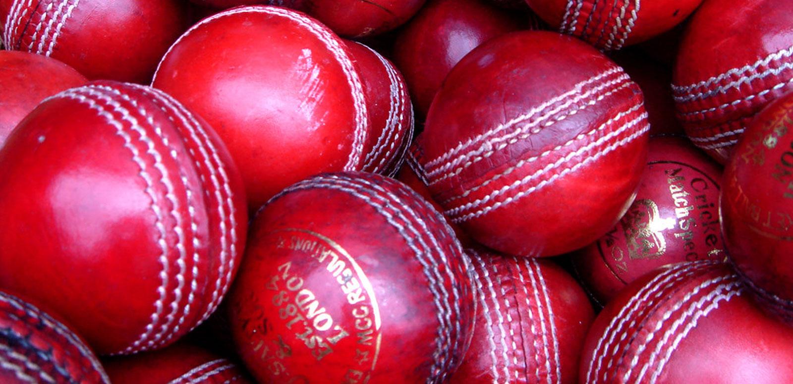 A close up of a collection of new and used red cricket balls inside a basket.