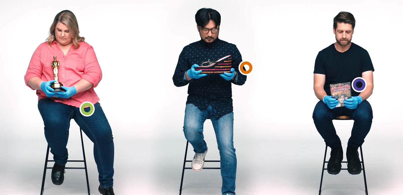 Three NFSA staff seated on stools and holding artefacts from the collection: an Oscar, a platform shoe and a video game