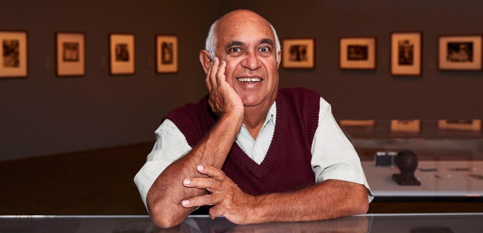 Portrait of Mervyn Bishop sitting at a counter with framed photos in the background.