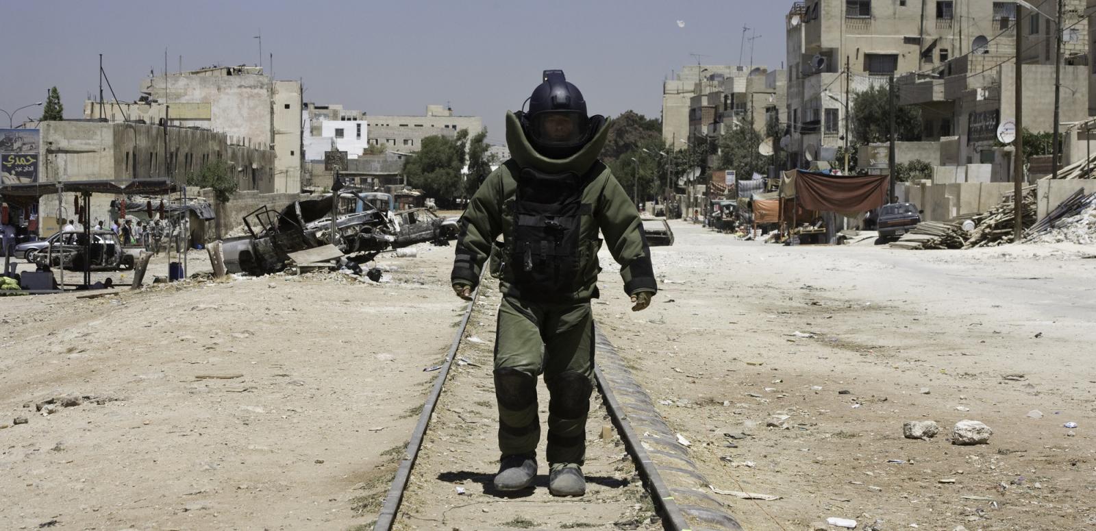 A lonely figure wearing bomb disposal protection walks toward the camera. A lonely figure wearing bomb disposal protection walks toward the camera.