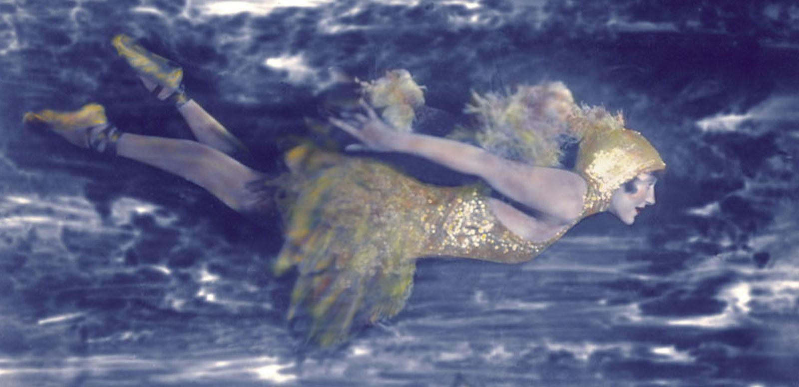 Annette Kellerman - exhibition hero - swimming Hand-tinted photograph of Annette Kellerman swimming underwater wearing an elaborate costume including ballet slippers and head-dress.