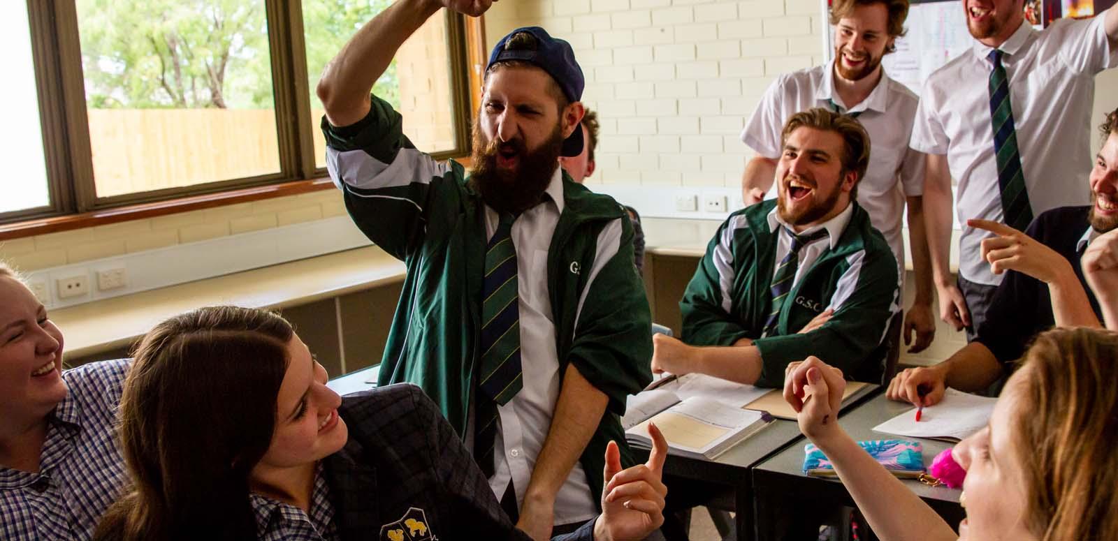 A group of high school students in uniform (including an older man with a beard) laughing and gesticulating 