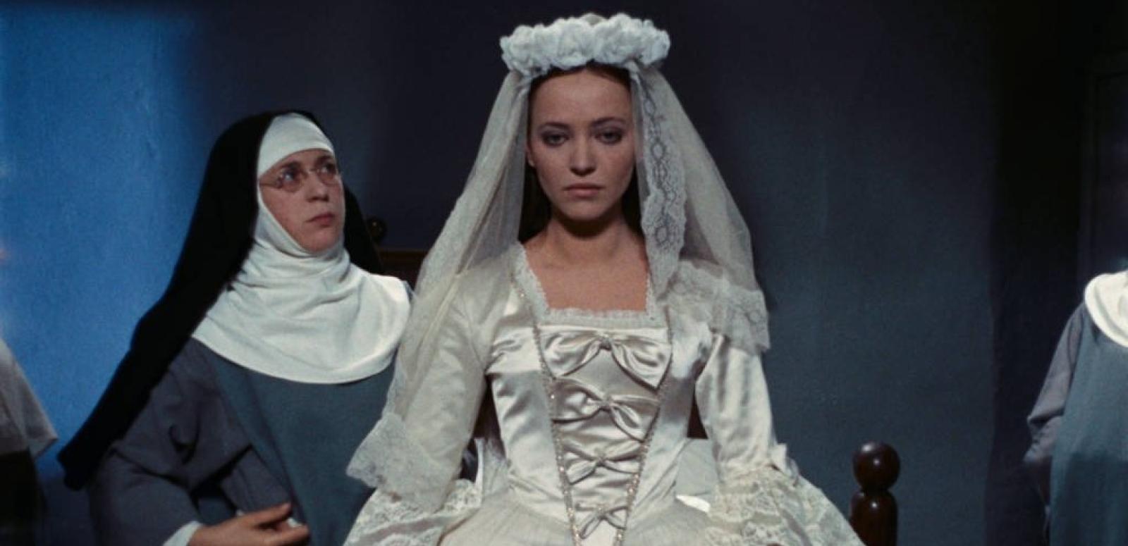 A young woman in a wedding gown stands centre of frame while a nun to her right looks at her intensely
