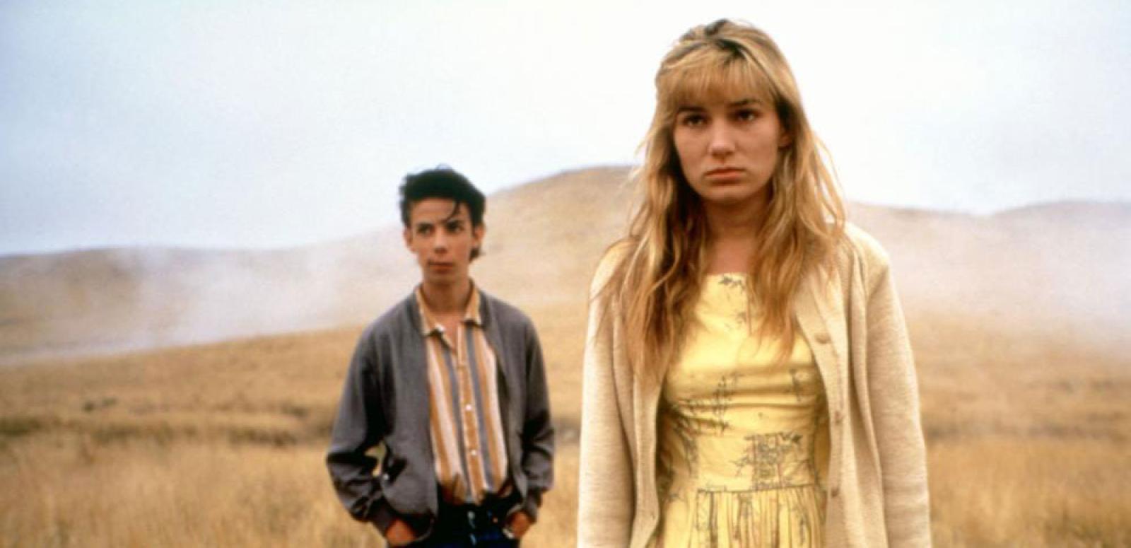 A young girl stands in a barren landscape looking forlorn with a boy standing some distance behind her. A young girl stands in a barren landscape looking forlorn with a boy standing some distance behind her.