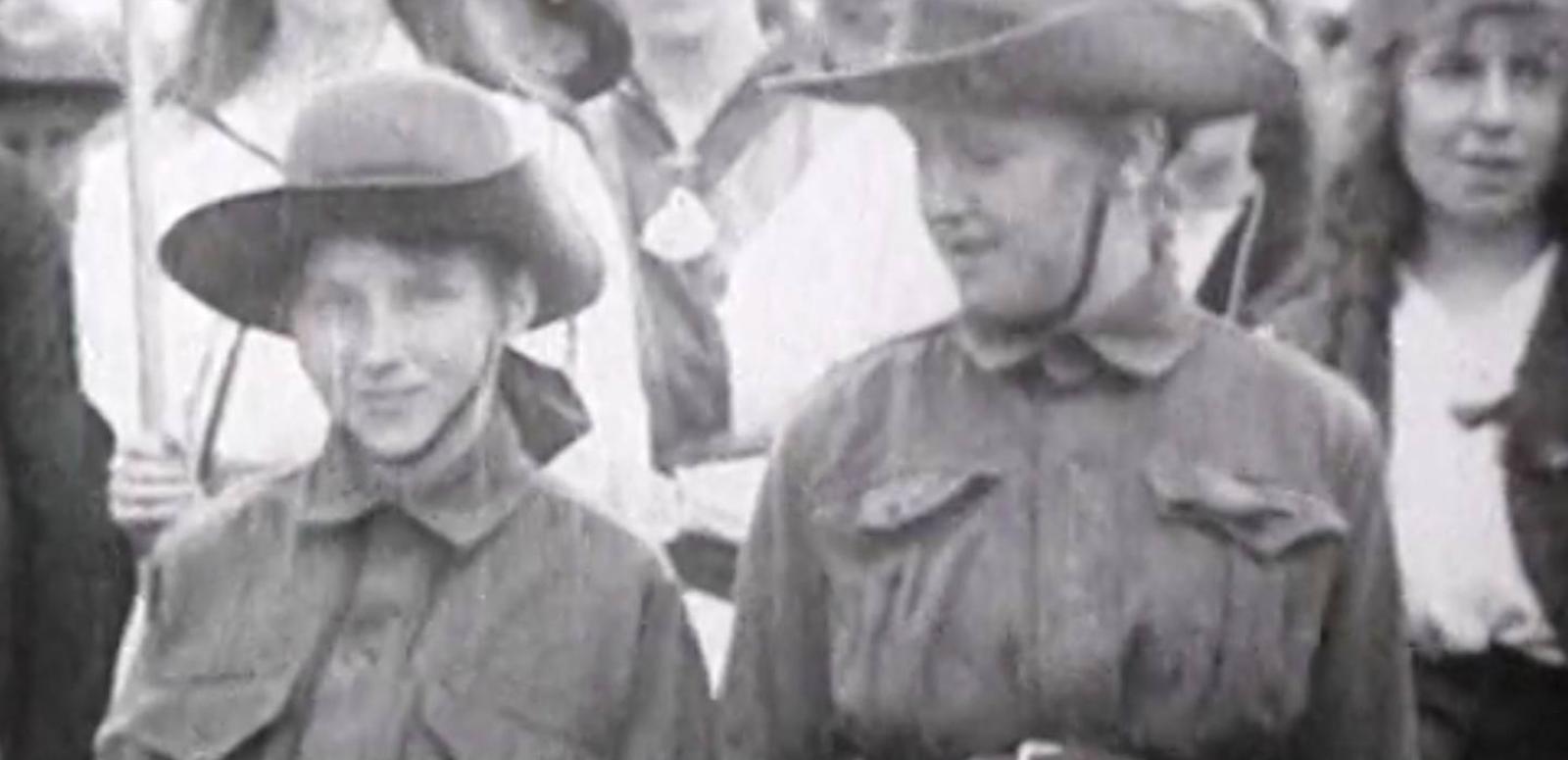 Two boys in soldiers' uniforms at an Anzac Day stand with a crowd of people at the first Anzac Day commemoration