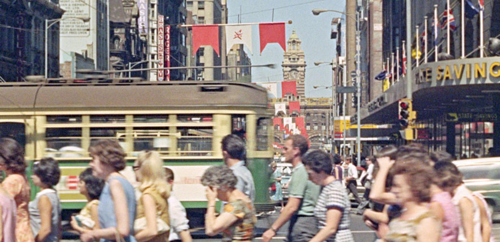 A busy street in Melbourne city with pedestrians and a tram going past.