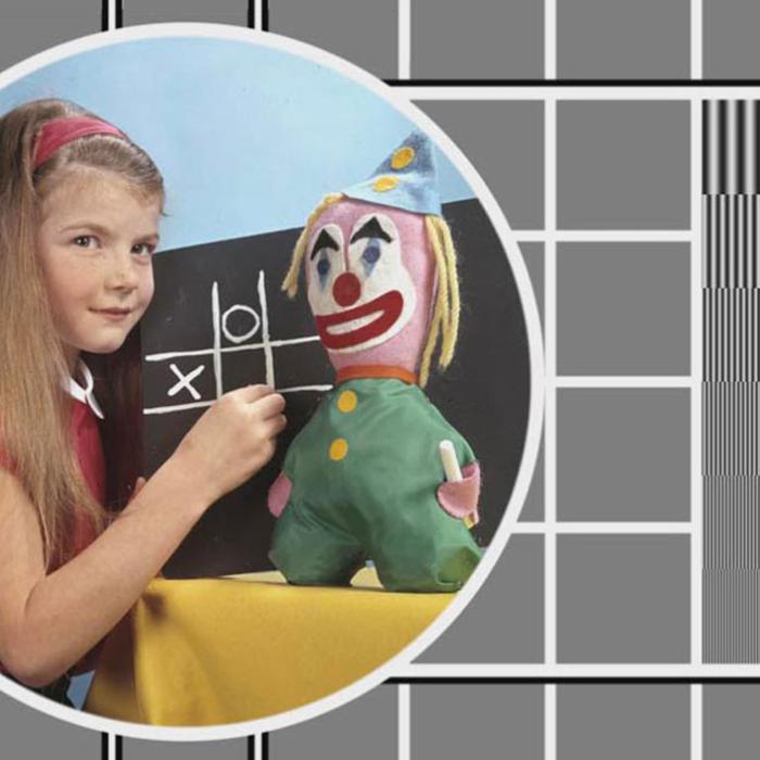 A colour TV test pattern with an inset image of a young girl in front of a chalkboard with a toy clown beside her