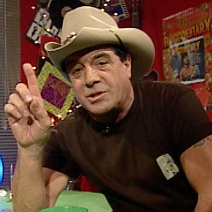 Music television presenter Ian 'Molly' Meldrum seated, wearing a hat, and holding one hand up and pointing his index finger. 