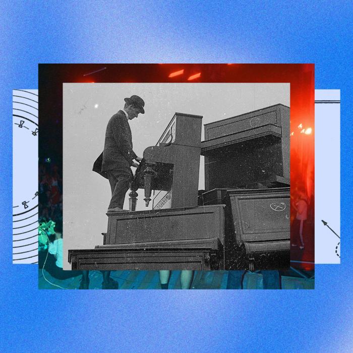 A man in a suit and bowler hat plays an upright piano while standing on another piano