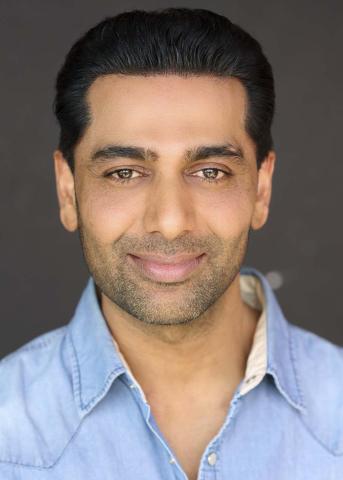 Sachin Job wearing a blue shirt with an open collar and smiling at the camera