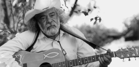 First Nations singer-songwriter Bob Randall playing a guitar outside