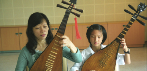 A woman and child each playing traditional Vietnamese Bau instruments at the Ha Noi National Conservatory of Music